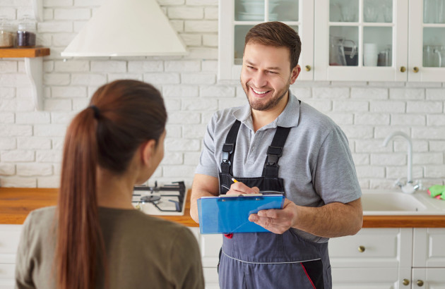 Technicien échangeant avec une cliente dans une cuisine lors d’une visite d’entretien d’un équipement de chauffage.