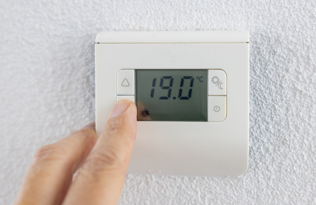 Main qui utilise un thermostat mural, température réglée à 19°C