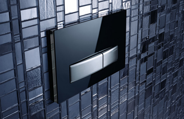 Plaque de commande de chasse d’eau encastrée noire et chrome sur mosaïque sombre.