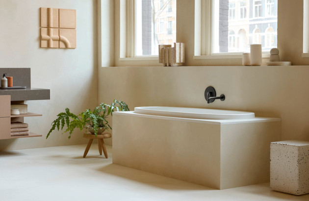 Baignoire encastrée habillée d’un revêtement ton pierre dans une salle de bains chaleureuse aux lignes épurées.