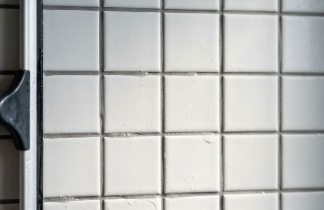 Gros plan sur un carrelage mural blanc carré avec joints gris dans une salle de bains moderne.