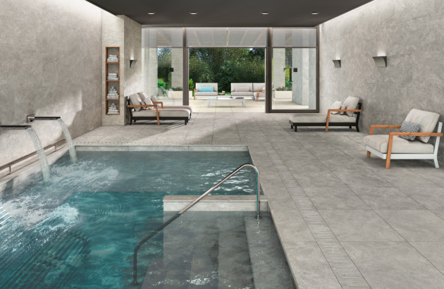 Espace spa intérieur avec piscine et carrelage travertin gris antidérapant, parfait pour une ambiance relaxante et naturelle.