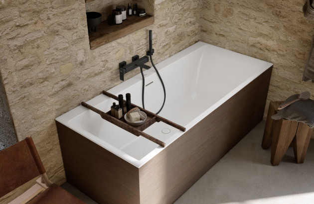 Baignoire rectangulaire style Japandi avec tablier bois, robinetterie noire mate et murs en pierre naturelle pour une ambiance zen.
