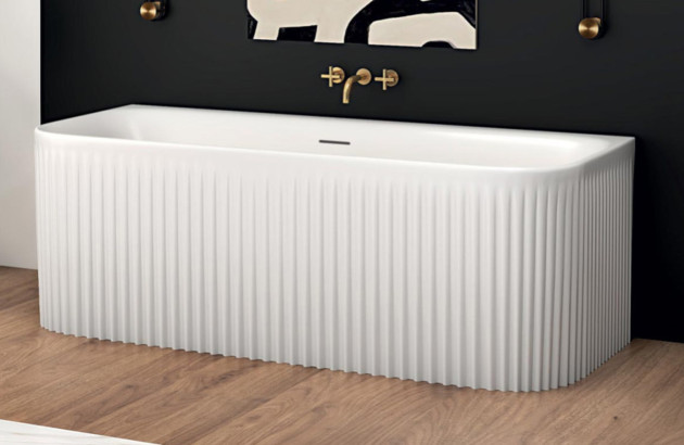 Baignoire îlot à façade cannelée blanche dans une salle de bains contemporaine aux accents noirs et dorés.