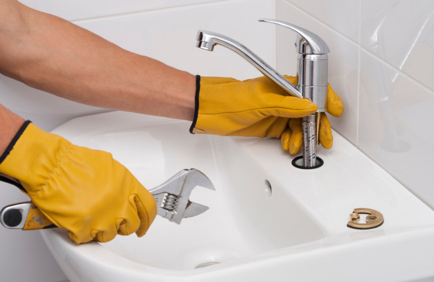 Personne qui démonte son robinet avec des gants jaunes