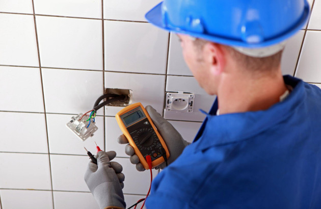 Électricien utilisant un multimètre pour vérifier une prise murale dans une salle de bains en rénovation.