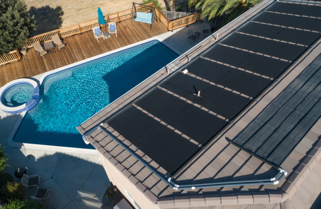 Vue aérienne d'un toit de maison avec des panneaux solaires et une grande piscine en contrebas