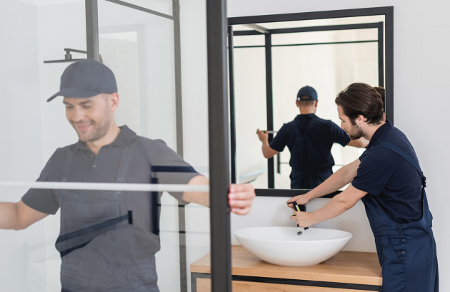 installateurs en plein travail dans une salle de bain qui ajustent une paroi de douche en verre et un robinet sur une vasque