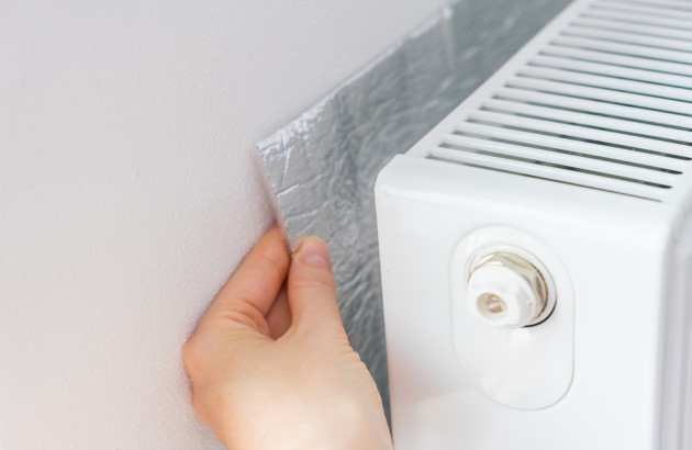 Personne qui tient une plaque isolante derrière un radiateur électrique