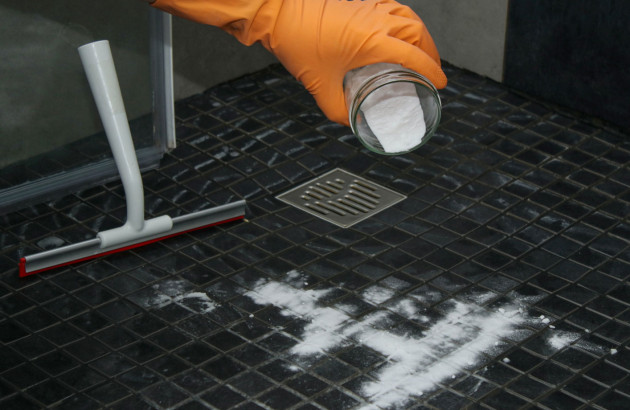 Homme avec un gant orange qui met du produit sur son carrelage de douche pour le nettoyer