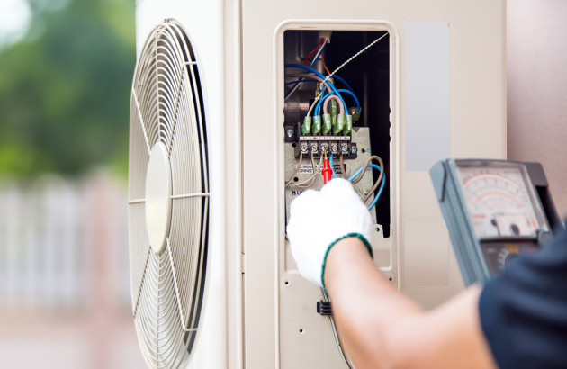 Technicien réalisant le contrôle électrique et la maintenance d’une unité extérieure de climatisation.