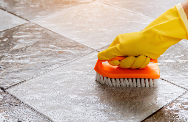 Homme avec un gant jaune qui utilise une brosse pour nettoyer des carreaux de carrelage au sol