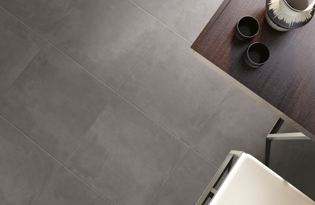 Carrelage gris foncé en grand format, vue rapprochée sur les joints et le plateau d’une table, effet matière.