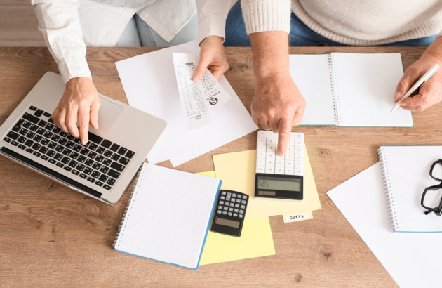 Deux personnes qui font des calculs avec un ordinateur portable, une calculatrice et des carnets de notes