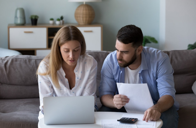 Couple qui regarde un ordinateur et tien des feuilles de papier assis dans un canapé