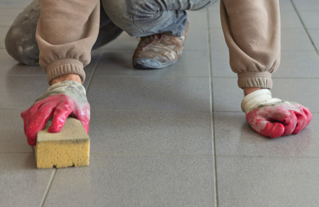 Homme au sol avec des gants qui passe l'éponge sur le carrelage