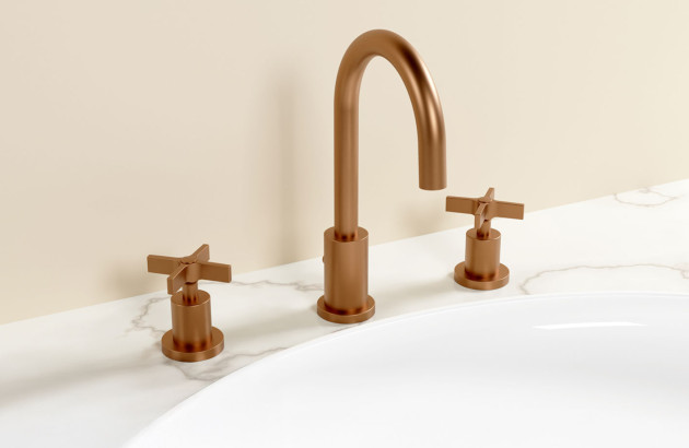 Robinetterie trois trous finition cuivre brossé sur un lavabo blanc avec design moderne et épuré.