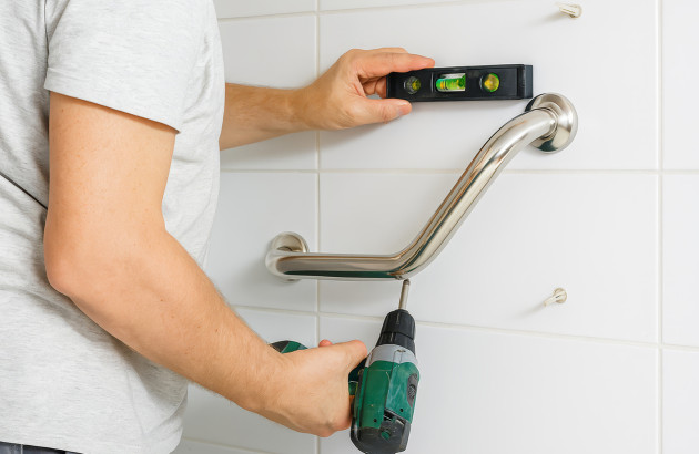 Artisan qui installe une barre de maintien sur un mur