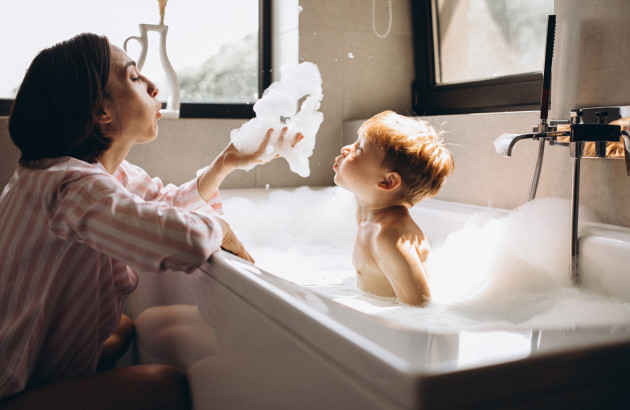 Femme qui joue avec un petit garçon dans une baignoire pleine de mousse