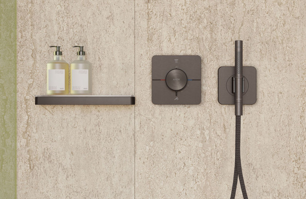 Commande de douche encastrée noire mate avec douchette à main assortie dans une douche au design minimaliste.