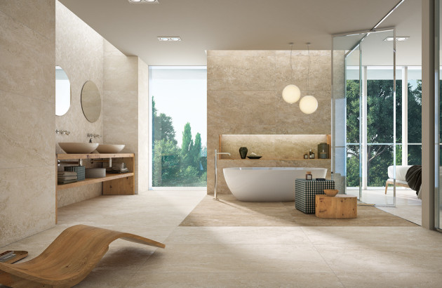 Salle de bains lumineuse avec sol et murs en grès cérame beige, baignoire îlot et double vasque en bois.