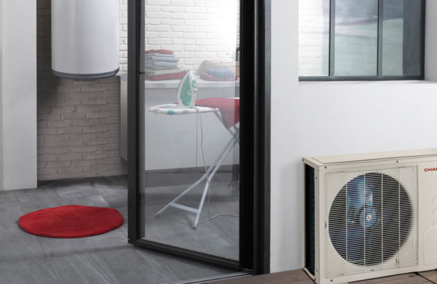 Maison avec une porte ouverte et une unité extérieure de pompe à chaleur installée à sa droite