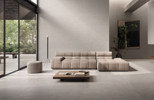 Grand salon minimaliste avec sol gris grand format façon grès cérame, lumière naturelle et baie vitrée.