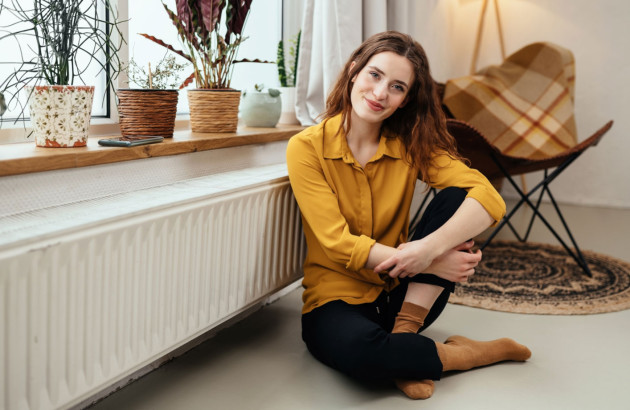 Femme assise près du radiateur sous la fenêtre ensoleillée