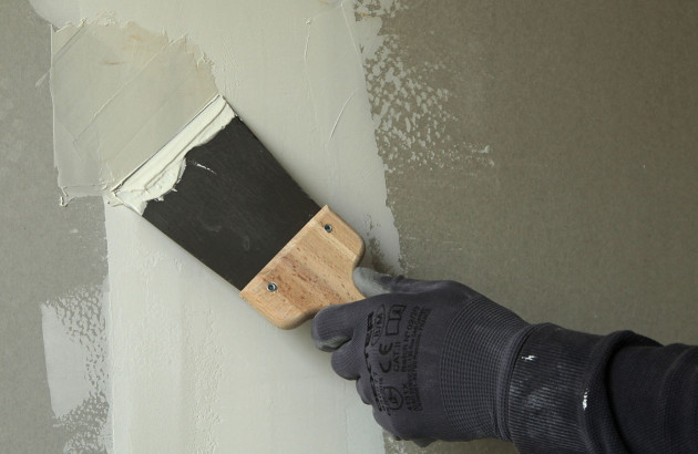 Un peintre utilise une spatule pour appliquer de la peinture sur un mur.