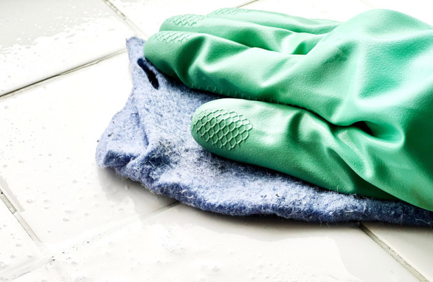 Gants verts qui nettoient des carreaux de carrelage avec un chiffon