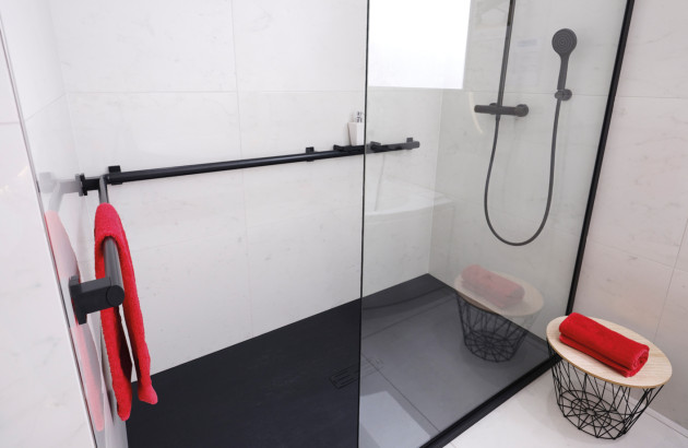 Douche à l’italienne avec paroi en verre, barre d’appui noire et sol antidérapant.