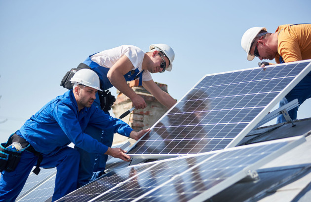 Trois artisans chargés d'installer des panneaux solaires sur un toit