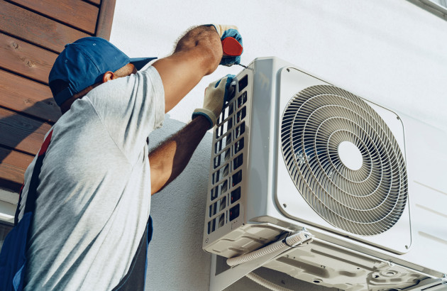 Installateur fixant une unité extérieure de climatisation murale