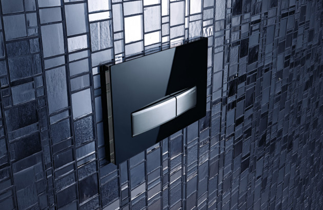 Plaque de commande design pour WC suspendu sans bride, finition noire brillante avec double bouton poussoir, intégrée dans un mur carrelé effet mosaïque.