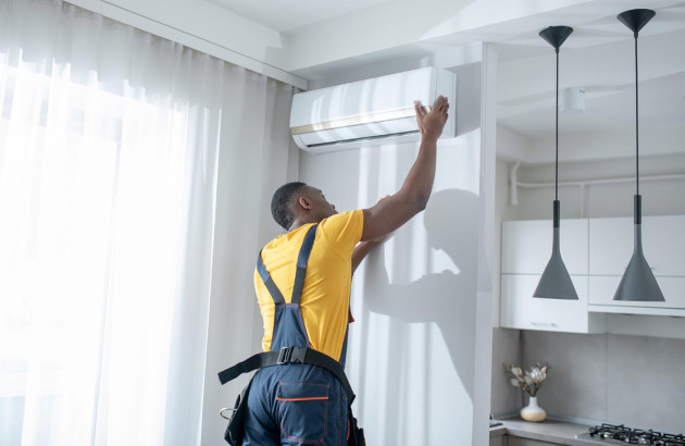 technicien en salopette et t-shirt jaune qui est en train de régler ou installer un climatiseur mural blanc dans une cuisine