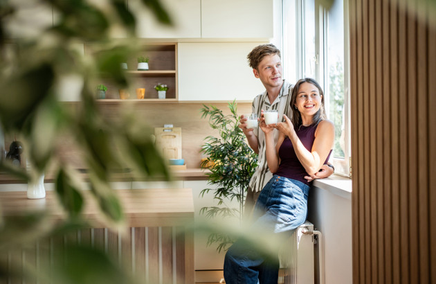 Jeune couple qui boit des verres de lait et regarde par la fenêtre en s'appuyant sur leur radiateur