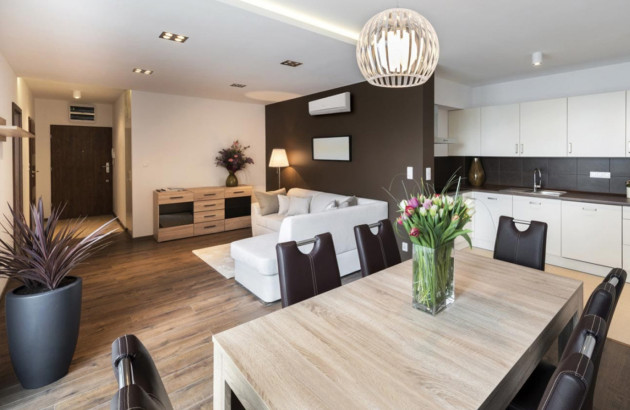 Salon contemporain ouvert sur une cuisine blanche, équipé d’une climatisation murale au-dessus du canapé.