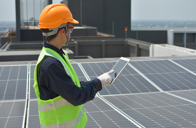 Homme avec un gillet jaune sur le toit d'un immeuble recouvert de panneaux solaires