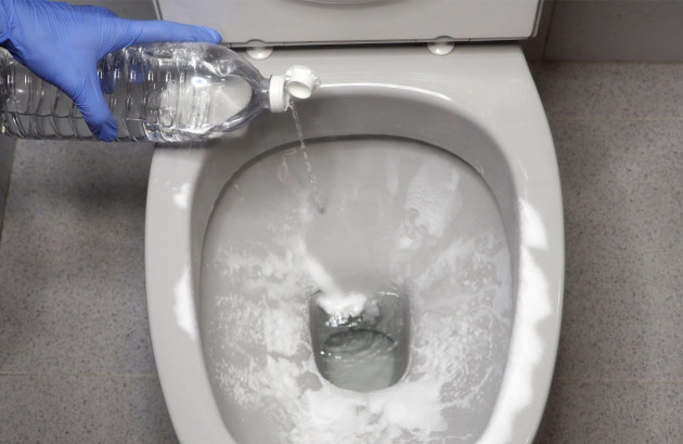 Personne qui ajoute du vinaigre blanc sur du bicarbonate de soude dans des toilettes