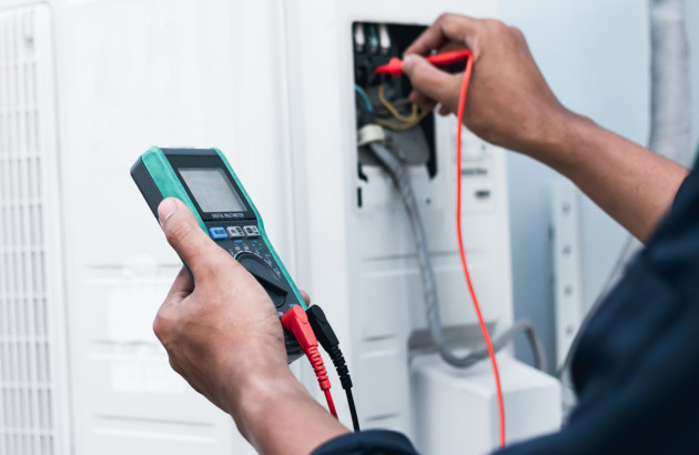 Technicien contrôlant les raccordements électriques d’un équipement de chauffage à l’aide d’un multimètre.