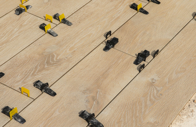 Installation de carreaux imitation bois avec croisillons de nivellement pour une pose précise.