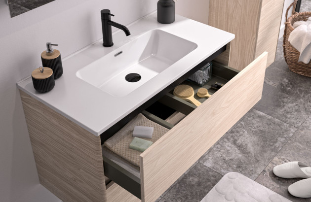 Gros plan sur un meuble sous vasque avec tiroir de rangement ouvert révélant une organisation optimisée des accessoires de toilette.