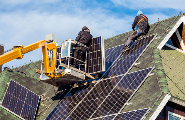Plusieurs personnes qui posent des panneaux solaires sur le toit d'une maison