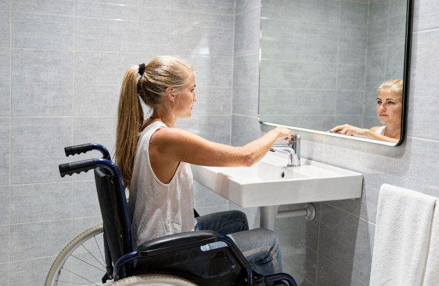 Personne en fauteuil roulant utilisant un lavabo adapté dans une salle de bains PMR