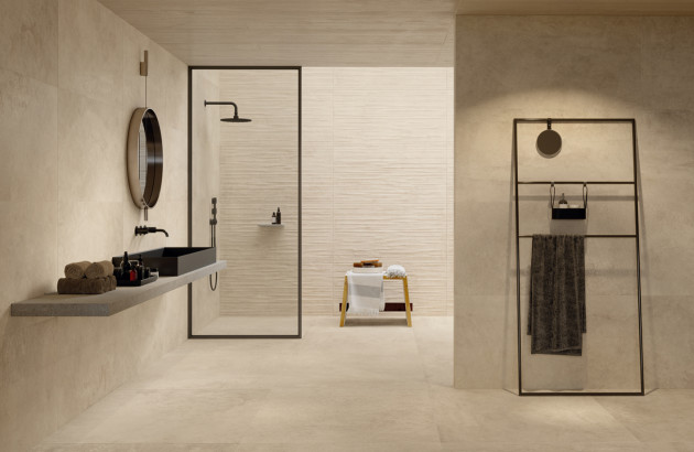 Salle de bains minimaliste aux tons beige, avec carrelage grand format effet pierre, douche à l’italienne et vasque noire à poser.