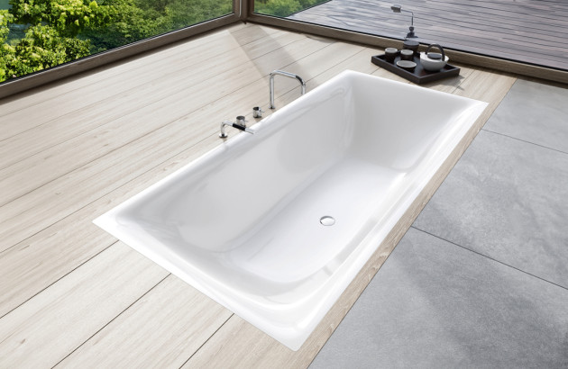 Baignoire encastrée blanche dans une salle de bains Japandi, sol effet bois clair, robinetterie chrome et vue nature.