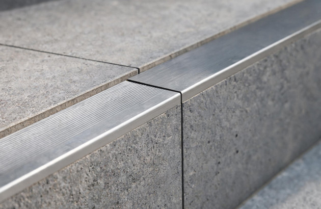 Détail d’un profilé de nez de marche en aluminium strié installé sur un escalier en carrelage gris.