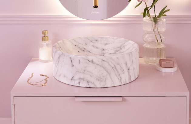Vasque en marbre blanc veiné installée dans une salle de bains aux tons rosés.