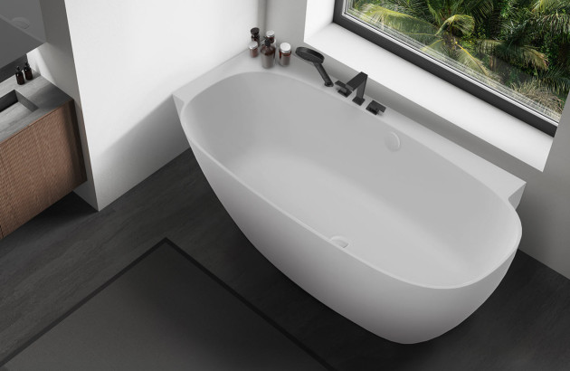 Baignoire îlot ovale blanche installée sous une fenêtre avec vue sur la végétation.