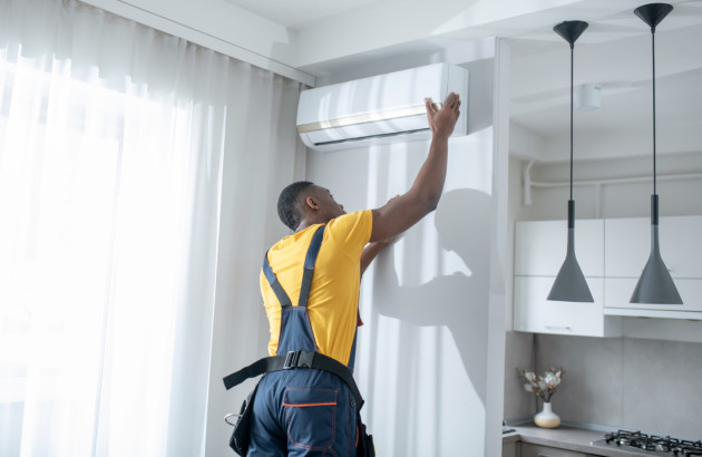 Technicien installant une unité intérieure de climatisation dans un salon moderne lors d’une installation de climatisation.